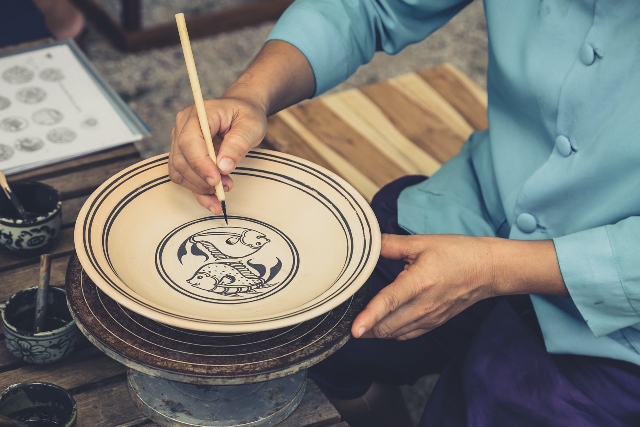 Artisan shaping traditional Sukhothai celadon pottery on a wheel in a local craft workshop
