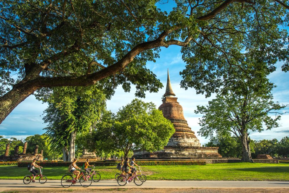 Cyclist on a quiet road through the Sukhothai countryside — rice fields and temple ruins in the distance