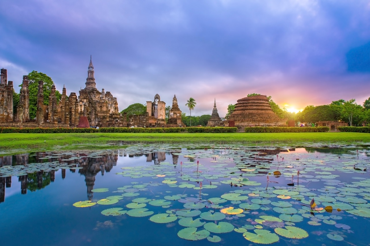 Sukhothai Historical Park at sunrise — stone temples rising above lotus-filled moats in morning mist