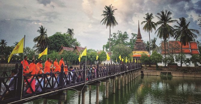 Morning alms procession — saffron-robed monks walking a quiet Sukhothai street at dawn