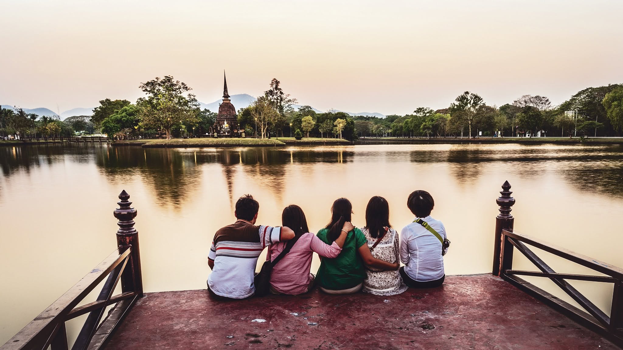 Friends taking in the view across the water at dusk, near the Tha Nam Rap Sadet market promenade in Sukhothai